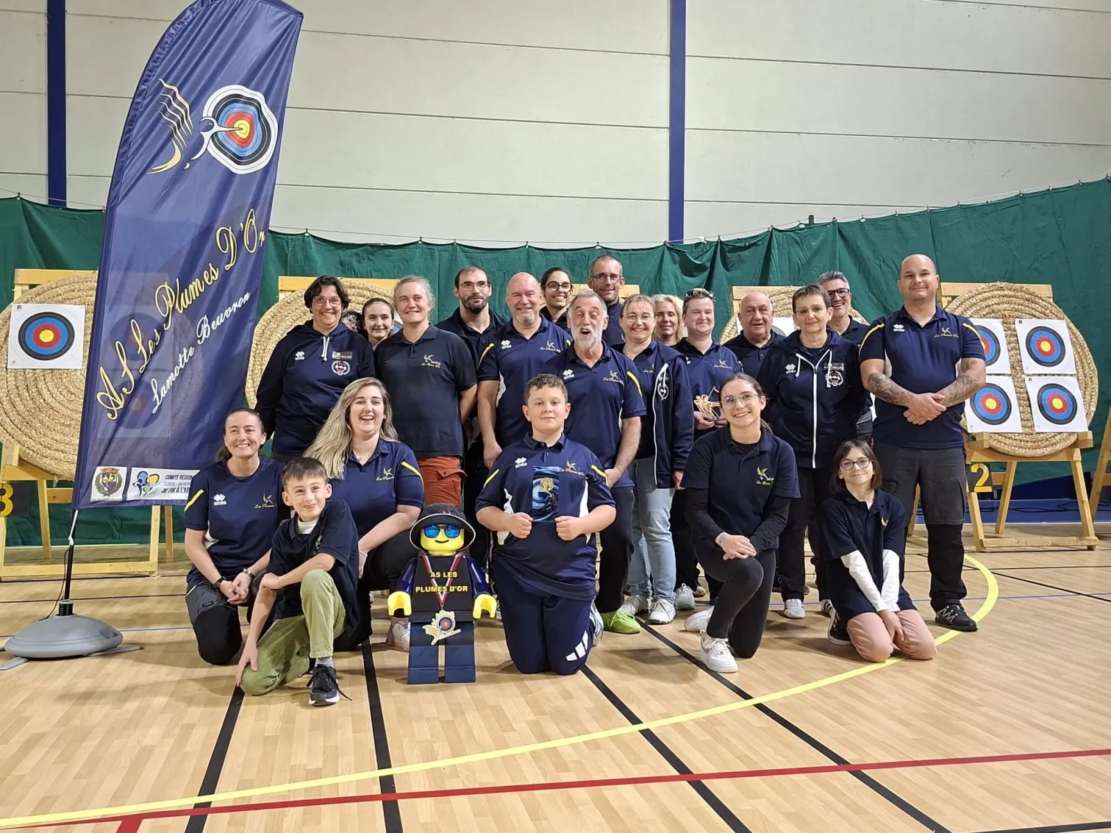Les archers du club As Les Plumes d'Or réunis dans le gymnase devant la banderole et les cibles
